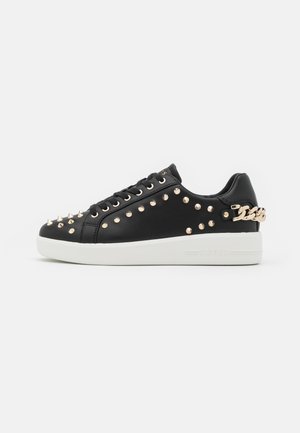 Schwarze Leder-Sneaker mit goldfarbenen Nieten, einer dekorativen Kette an der Ferse, runder Spitze und einer weißen Gummisohle.
