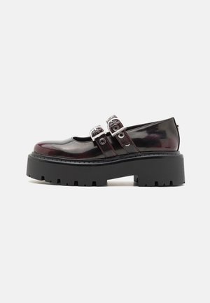 Black patent leather shoes with two adjustable buckle straps, featuring a chunky textured sole and rounded toe design.