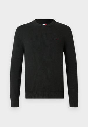 Black long-sleeve crewneck sweater with a small red, white, and blue flag logo on the left chest and ribbed cuffs and hem.