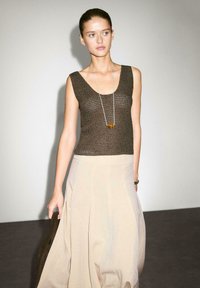 Brun strik tanktop med en scoop neck, parret med en lys beige, plisseret maxiskirt. Sølv halskæde med en cirkulær vedhæng, minimalistisk design.