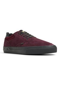 Burgundy suede sneaker with black accents, textured surface, gold eyelets, and contrasting black rubber sole. Low-profile design.