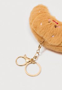 Porte-clés en forme de croissant en peluche orange doux, décoré de sprinkles colorés brodés et avec des anneaux et un fermoir en métal doré sur fond blanc.