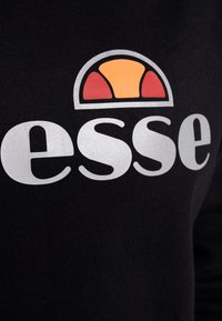 Sudadera negra con un gran logo blanco que incluye un diseño circular en naranja y rojo encima del texto "esse". Textura suave.