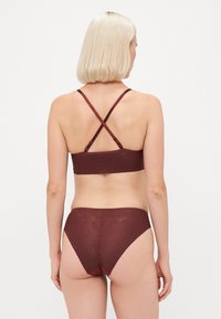Conjunto de sutiã e biquíni cor bordô com alças cruzadas, tecido texturizado e design de cintura alta; acabamento suave e material elástico.