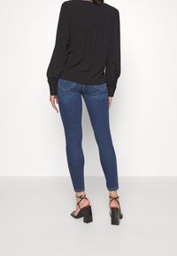 Slim-fit blå denimjeans med medelhög midja, som har bakfickor och en jämn, lätt blekt textur. Matchas med en svart blus.