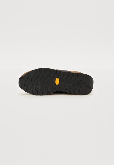 Semelle de chaussure de randonnée noire et brune avec des profondeurs, présentant un logo jaune proéminent et une surface texturée pour un meilleur grip.