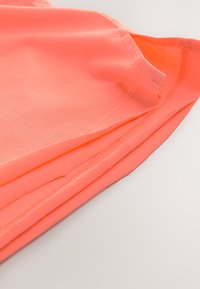 Maglietta in cotone arancione neon piegata con maniche corte. Il tessuto ha una texture liscia e presenta una scollatura rotonda. Nessun motivo o grafica.