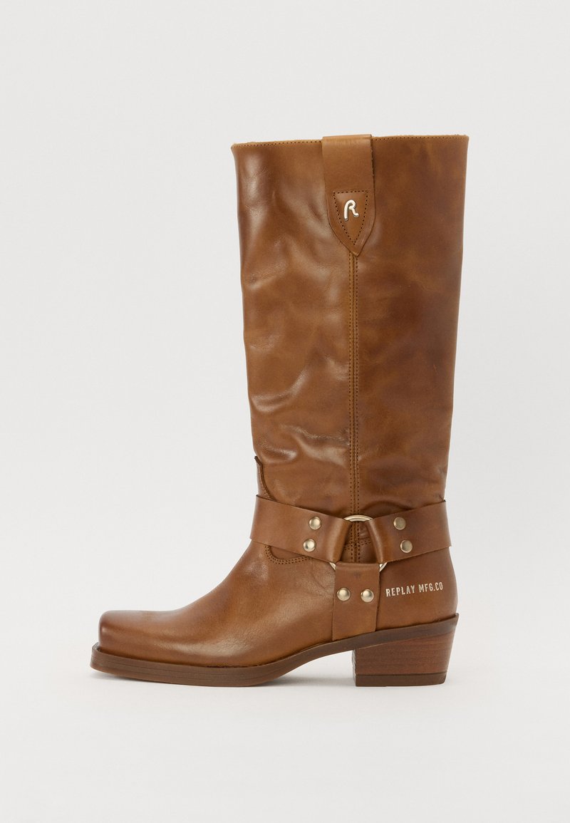 Bottes en cuir marron montantes avec un design flou, dotées d'une sangle avec quincaillerie métallique et d'un talon bloc. Texte "REPLAY MFG.CO" sur le côté.