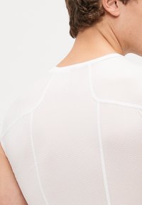 Hvid skjorte med korte ærmer i et tekstureret mesh materiale, med synlige sømme og en rund halsudskæring, vist fra bagsiden.