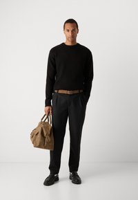 Pulover negru din tricot cu model înălțat, curea bej, pantaloni negri croiți, geantă din piele maro cu buzunare laterale și pantofi negri cu talpă groasă.