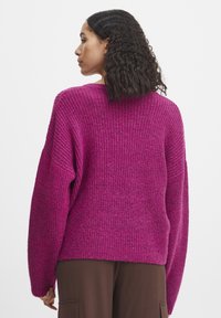 Pull en maille côtelée fuchsia avec une coupe décontractée, des épaules tombantes et des manches longues. Tissu texturé ; la vue de dos met en valeur l'ourlet et les coutures.