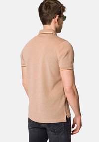 Beżowa koszulka polo z krótkimi rękawami, z kontrastowymi wykończeniami przy kołnierzyku, teksturowanym materiałem oraz bocznymi rozcięciami dla wygody.