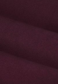 Tissu bordeaux avec une finition texturée et tissée, présentant une apparence lisse et une profondeur subtile, avec des tissages visibles et une couleur uniforme.