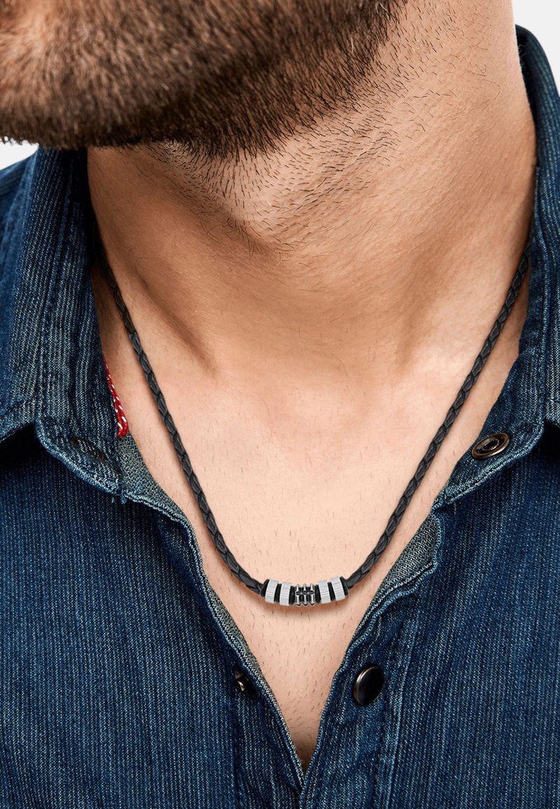 Collana in pelle nera intrecciata con accenti metallici, indossata sopra una camicia di denim, che mette in risalto il collo e l'area del collo di un uomo.