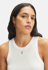 Orecchini con design rettangolare in metallo color oro rosa, indossati con una maglietta bianca a coste. È visibile anche una collana con pendente coordinato.