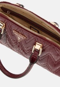 Bordeaux håndtaske med en tekstureret overflade, guldfarvede hardware og lynlås-lukning. Har et logo-plade og dobbelte top-håndtag.