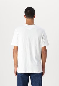 Hvit bomull t-skjorte med korte ermer og V-formet detalj bak, sammen med blå denimjeans. Jevn tekstur, avslappet passform.