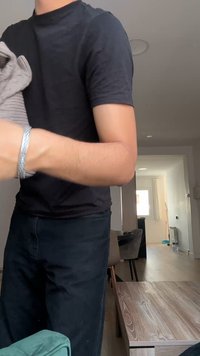 Personne en chemise et pantalon noirs tient une serviette grise pliée dans un salon moderne avec une table et des chaises en bois.