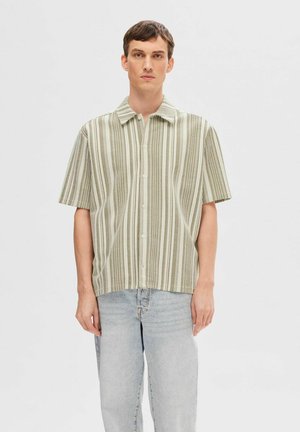 Grøn- og cremefarvet stribet kortærmet skjorte lavet af letvægtsstof, med knaplukning foran og en afslappet pasform. Jeans båret underneath.
