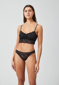 Zwart kanten lingerie-set bestaande uit een cropped top met scalloped randen en verstelbare bandjes, gecombineerd met bijpassende kanten string.