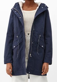 Parka azul marino con capucha forrada de piel, cierre de cremallera, cintura ajustable con cordón y dos bolsillos delanteros. Presenta detalles metálicos en plata.