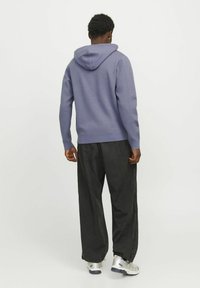 Lila Kapuzenpullover mit einer glatten Textur, kombiniert mit lockeren schwarzen Hosen. Das Outfit zeichnet sich durch ein lässiges, entspanntes Design aus.