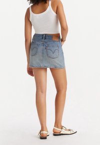 Lichtblauwe denim minirok met een rafelige zoom, voorzien van twee achterzakken en een bruine leren patch. Gecombineerd met een wit topje en sandalen.