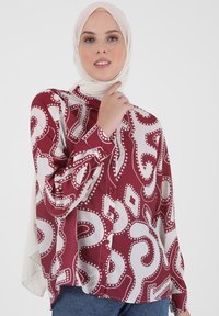 Bordeauxfarbener und cremefarbener Bluse mit Muster, Knopfverschluss, langen Ärmeln und lockerer Passform. Verfügt über ein wirbelndes Design mit kreisförmigen Akzenten.
