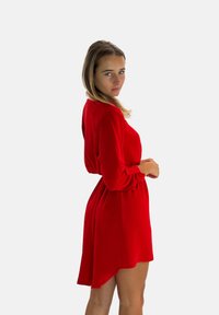 Robe rouge avec de longues manches froncées et une jupe évasée fluide. Fabriquée en tissu doux, elle présente un col haut et une texture subtile.