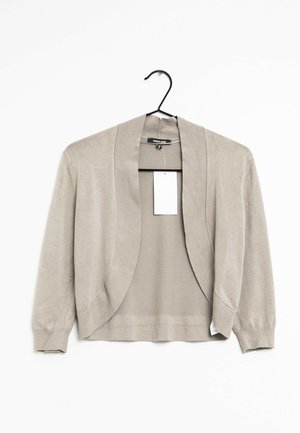 Beige cardigan hængende på en bøjle med en åben frontdesign, lange ærmer og en glat tekstur. En tøjlabel er synlig indeni.