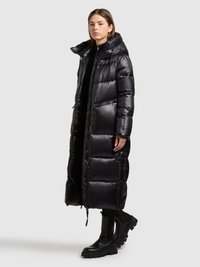 Cappotto lungo imbottito nero con collo alto, materiale lucido, tasche con zip e vestibilità comoda. Abbinato a stivaletti neri chunky.