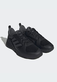 Zapatillas deportivas negras con una parte superior de malla texturizada, superposiciones sintéticas y un diseño de rejilla triangular en la suela. Presenta cordones y acentos negros.
