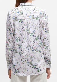 White long-sleeve shirt with a colorful floral and bird pattern worn by a person shown from the back against a plain background.