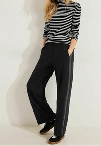 Zwarte wijde broek met een rechte snit, voorzakken en contrasterende zijstrepen. Gecombineerd met een zwart-wit gestreepte top.