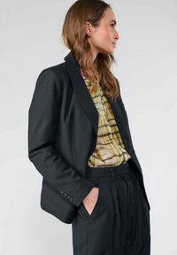 Zwarte pinstripe blazer van gestructureerde stof met een notch-kraag en één-knops sluiting, gecombineerd met een patroon top en broek.