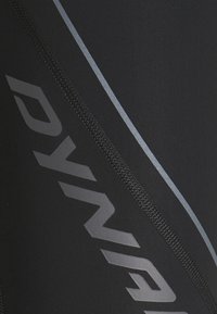 Čierne športové legíny s textúrovaným povrchom, ktoré majú výrazný strieborný pruh a sivé logo na ľavej strane. Obsahujú detaily so zipsom.