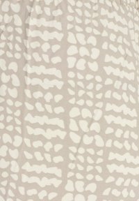 Tissu beige avec des taches blanches abstraites irrégulières ressemblant à un imprimé animal, montrant la texture et de légers plis.