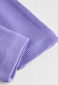 Tissu violet à côtes avec une texture subtile et une couture contrastante le long de l'ourlet, mettant en avant un gros plan du bord et du pli du vêtement.