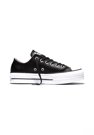 Sort lavtop sneakers med hvid tyk gummisål, sorte snørebånd, metaløjer og tekstureret tåhætte på hvid baggrund.