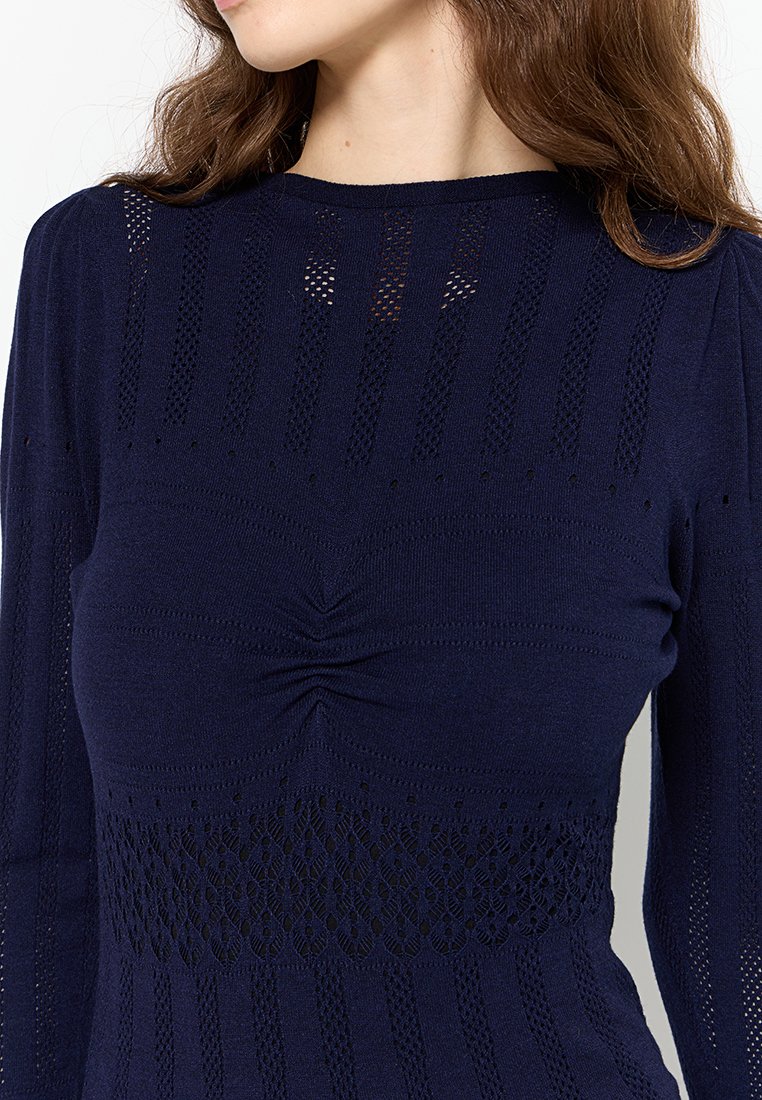 Haut tricot marine avec un design texturé, des motifs ajourés et un centre froncé. Manches longues avec des détails sophistiqués.