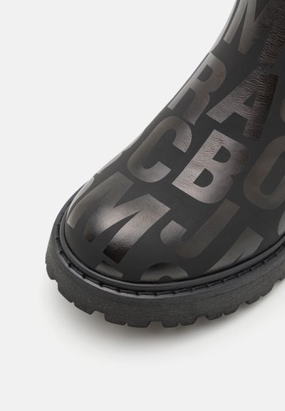 Svart gummistøvel til ankelen med en teksturert overflate med store bokstaver, en avrundet tå og en kraftig gripe såle.