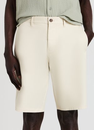 Pantaloncini beige in tessuto liscio, con pancia piatta, tasche laterali e chiusura con bottone. L'orlo è dritto e pulito.