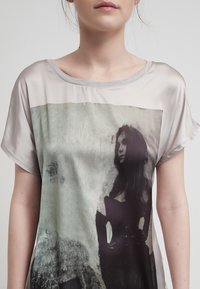 Camiseta de seda con un estampado gráfico en gris y negro que presenta una figura. Cuello redondo, mangas cortas y una textura suave.