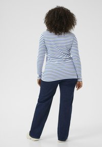 Long-sleeve, striped top in white and blue, paired with dark blue jeans. Casual fit, straight leg, and soft fabric texture.