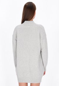 Ljusgrå överdimensionerad stickad tröja med hög krage, neddragna axlar och ribbad nederkant. Mjuk textur, når till mitten av låret.