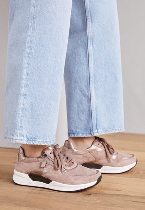 Lichtblauwe spijkerbroek gecombineerd met beige en metallic roze veterschoenen met witte zolen, staand op een houten vloer.