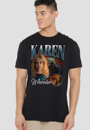 Junger Mann trägt ein schwarzes T-Shirt mit dem Schriftzug "Karen Wheeler" und drei Bildern einer blonden Frau mit verschiedenen Gesichtsausdrücken und Posen.