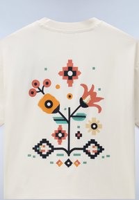 Κρεμ μπλουζάκι με πολύχρωμο αφηρημένο floral και γεωμετρικό pixel art σχέδιο στην πλάτη σε πορτοκαλί, μαύρο, πράσινο και μπεζ.
