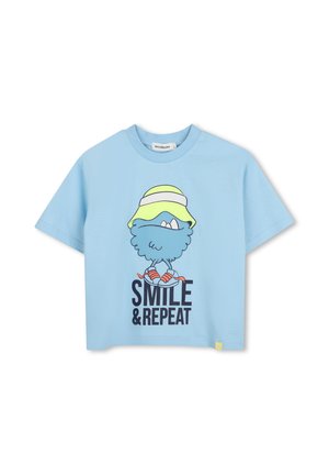 T-shirt bleu clair avec une créature bleue de dessin animé portant un chapeau jaune et des chaussures orange au-dessus du texte "SMILE & REPEAT".