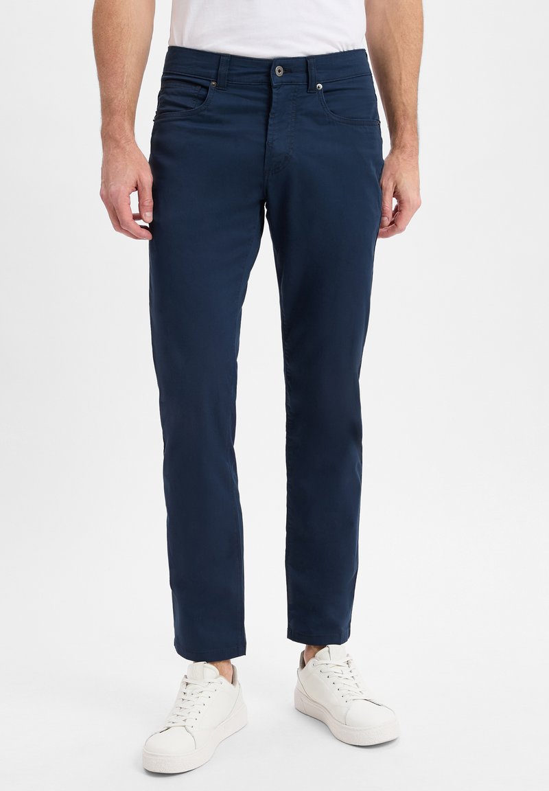 Navy Chinos aus einem glatten Stoff mit slim fit und Fünf-Taschen-Design. Mit einem Reißverschluss und Knopfverschluss, kombiniert mit weißen Sneakers.